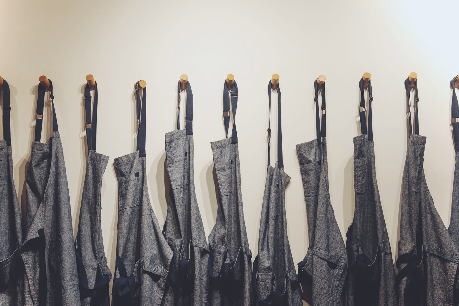 Row of denim work aprons hanging on wall hooks