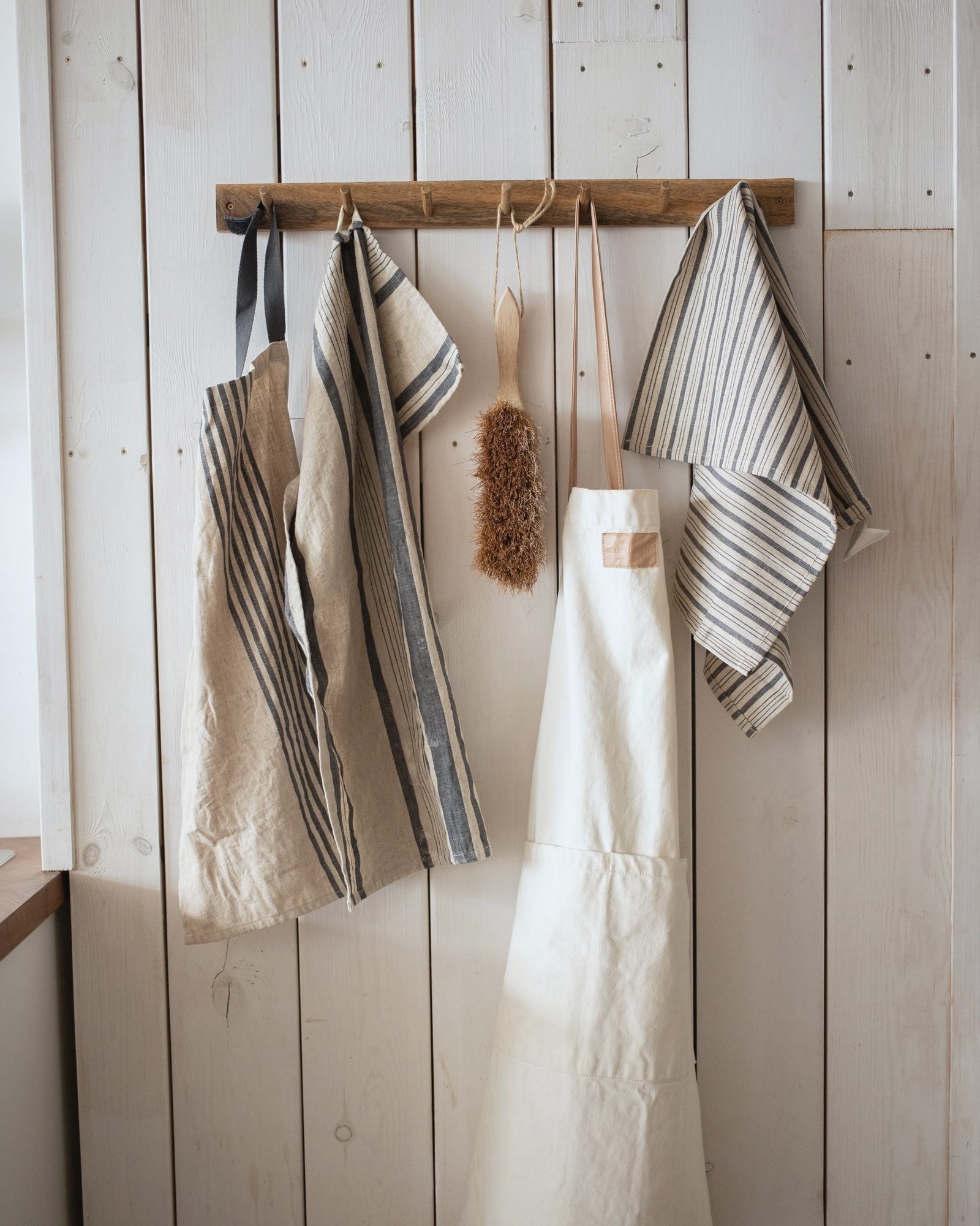 Aprons and indigo-striped towels hung on a wooden peg rail